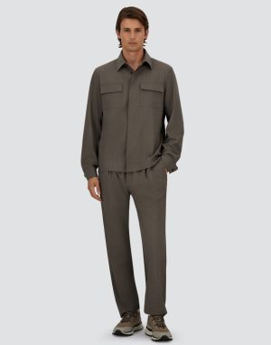 Man wearing a taupe-gray matching shirt and relaxed-fit pants with beige sneakers, standing against a light gray background.