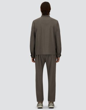 Back view of a person wearing a loose gray suit and matching trousers, standing against a light background, sneakers visible at the feet