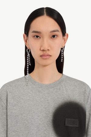 Close-up of a woman with straight black hair, wearing a gray sweatshirt and long crystal earrings.