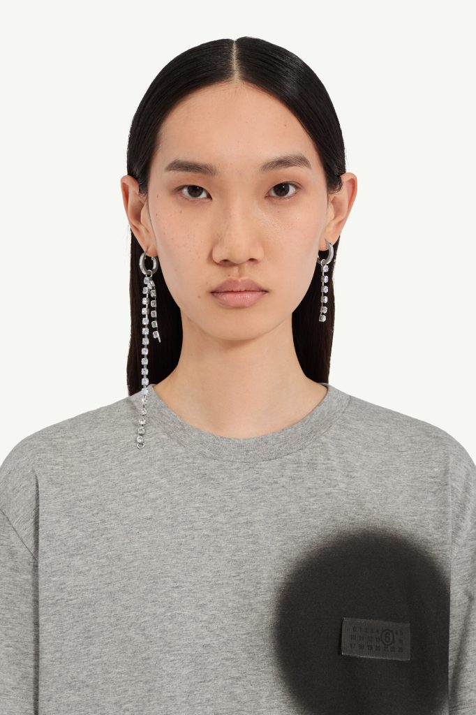 Close-up of a woman with straight black hair, wearing a gray sweatshirt and long crystal earrings.