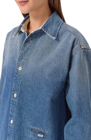 Close-up of a person wearing a light blue denim shirt with a pointed collar, visible buttons, and stitching.