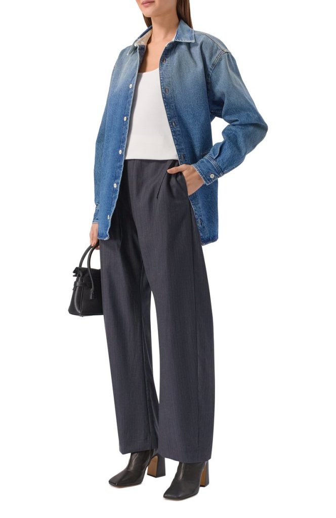 Model wearing a blue denim shirt/jacket over a white top with wide-leg dark gray trousers, black handbag, and black block-heel ankle boots.