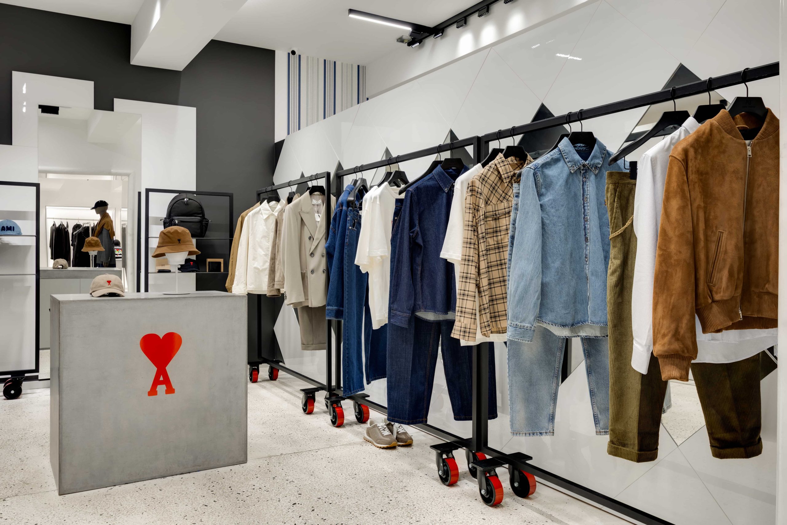 Clothing store interior with rows of jeans and jackets on rolling racks and a gray reception counter with a red heart logo in the foreground.