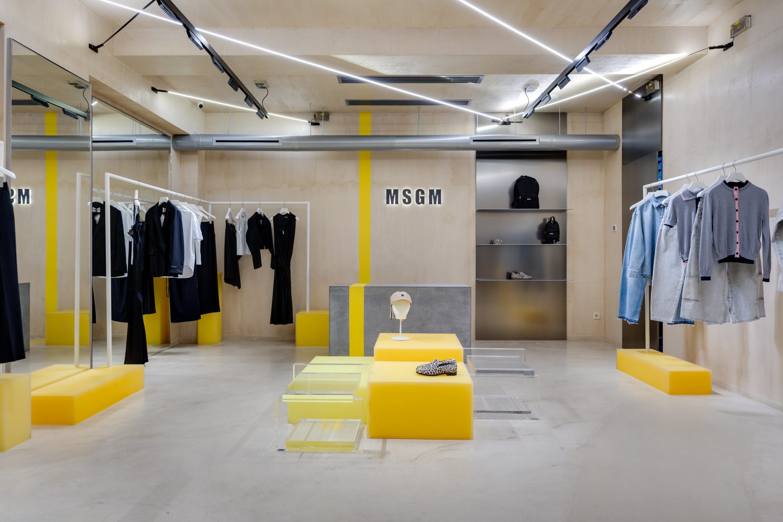 Interior of a MSGM clothing store with racks of dresses and jackets, and yellow display blocks.