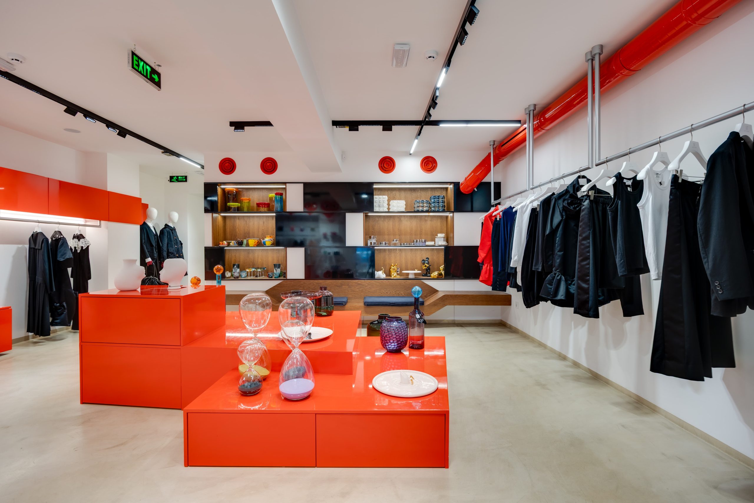 Modern clothing store interior with bright orange display tables and racks of black and white outfits on the right.