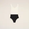 Flat lay of a white sleeveless top paired with a black high-waisted bottom on a pale beige background, forming a color-block swimsuit silhouette.