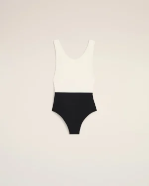Flat lay of a white sleeveless top paired with a black high-waisted bottom on a pale beige background, forming a color-block swimsuit silhouette.