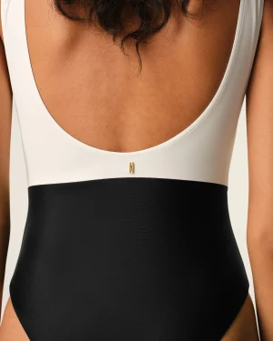 Back view of a person wearing a white sleeveless top with a black band around the lower torso; small gold vertical tag at the center back.