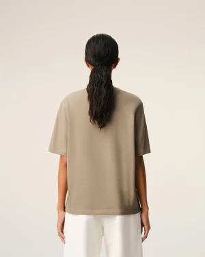 Back view of a person with long dark hair in a low ponytail, wearing a beige oversized T-shirt against a light neutral background.