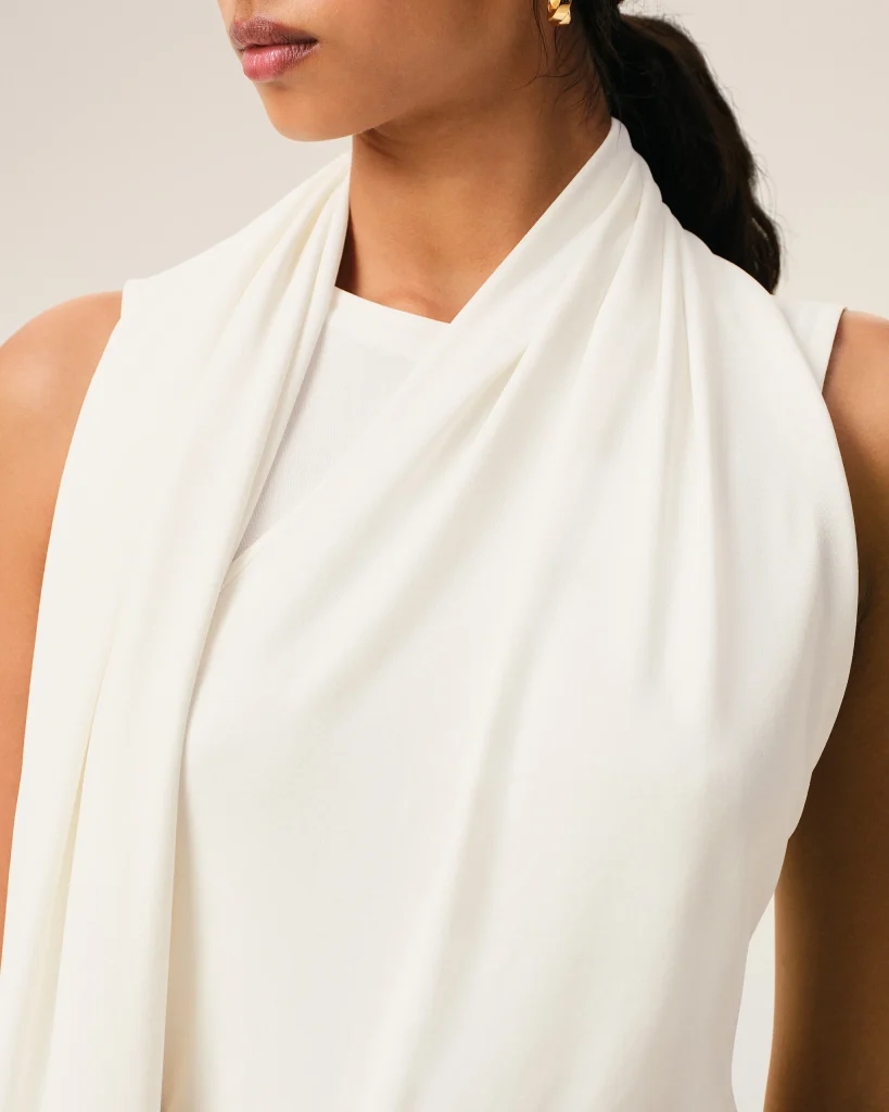 Close-up of a person wearing a white draped garment, showing lips and shoulder against a neutral background.
