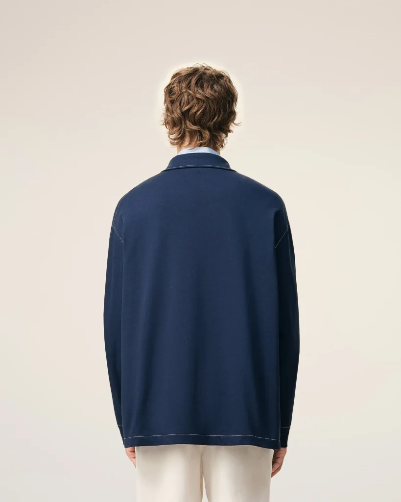 Back view of a person wearing a navy blue jacket with light beige pants against a pale background.