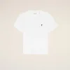 White t-shirt with a small black heart logo on the left chest against a pale peach backdrop.