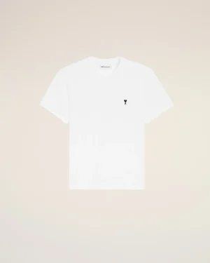 White t-shirt with a small black heart logo on the left chest against a pale peach backdrop.