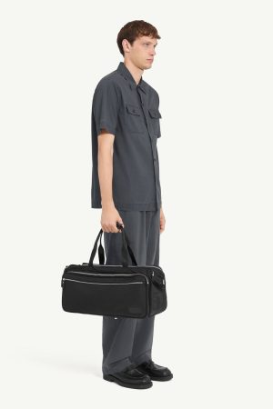 Side view of a man in charcoal gray shirt and matching pants carrying a black duffel bag with multiple zip pockets and handles