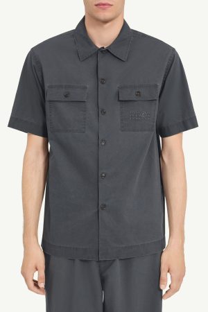 Dark gray short-sleeve button-down shirt with two chest pockets, each with a flap and button, worn by a person.