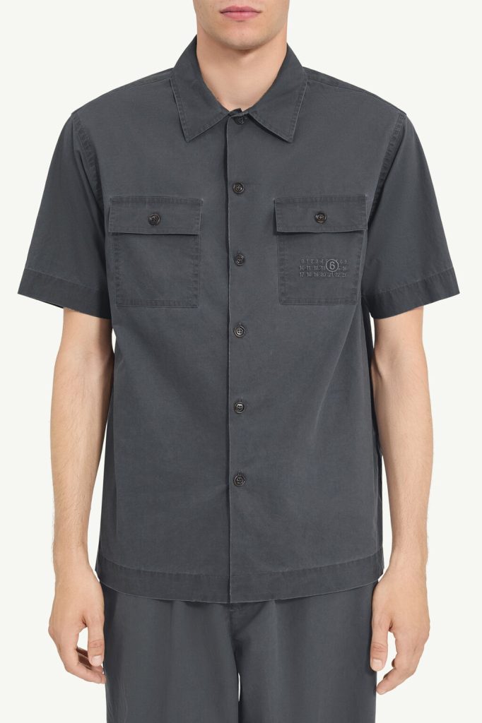 Dark gray short-sleeve button-down shirt with two chest pockets, each with a flap and button, worn by a person.