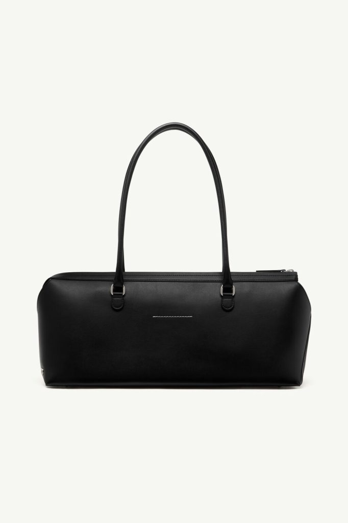 Black leather handbag with two top handles and a top zip closure, resting on a plain light background.