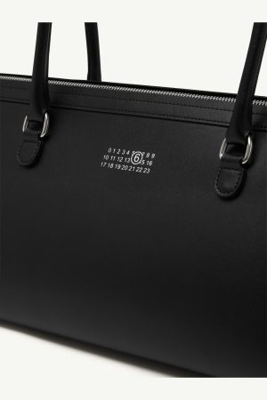 Close-up of a black leather handbag with a white numbered logo on the front surface.