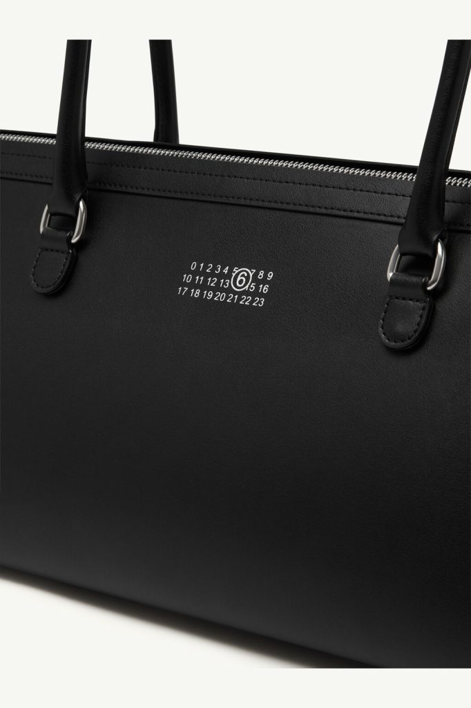 Close-up of a black leather handbag with a white numbered logo on the front surface.