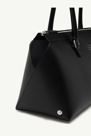 Close-up of a black leather handbag showing the corner, zipper top, handles, and a metal stud on the base.
