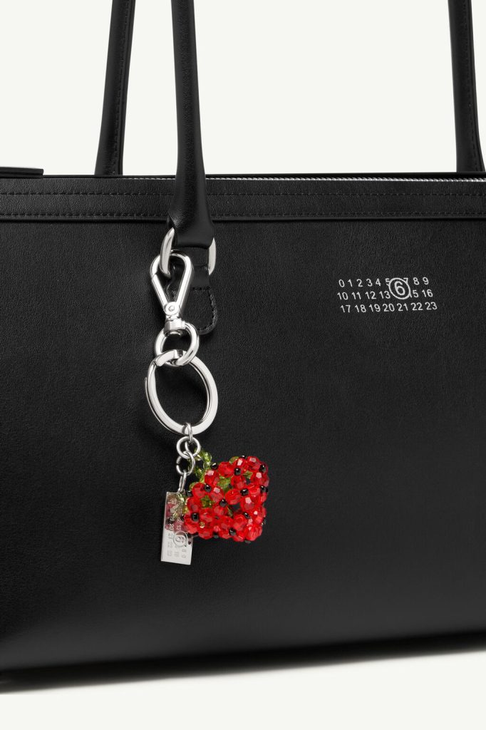 Close-up of a black leather handbag with a silver key ring and a red beaded heart charm hanging from a strap.