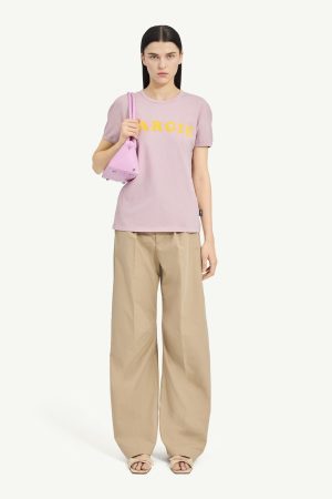 Woman wearing a pastel pink T-shirt with the word 'MARGIE' in yellow, paired with beige wide-leg pants and a pink shoulder bag.