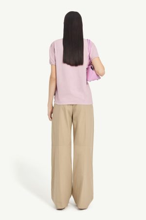 Back view of a person wearing a pastel pink T-shirt and beige wide-leg pants, carrying a pink handbag on the left shoulder.