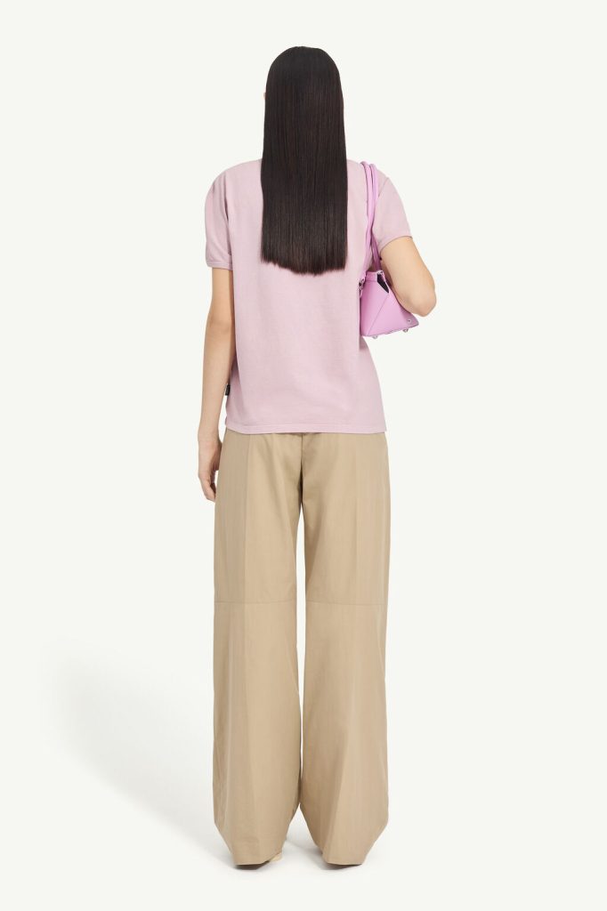 Back view of a person wearing a pastel pink T-shirt and beige wide-leg pants, carrying a pink handbag on the left shoulder.