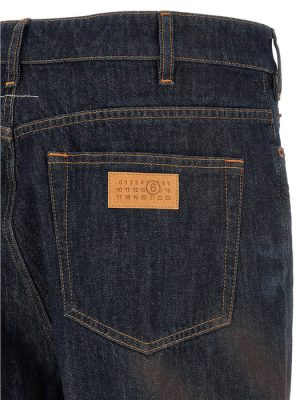 Back of dark denim jeans showing a rear pocket with a tan rectangular brand patch and orange stitching.