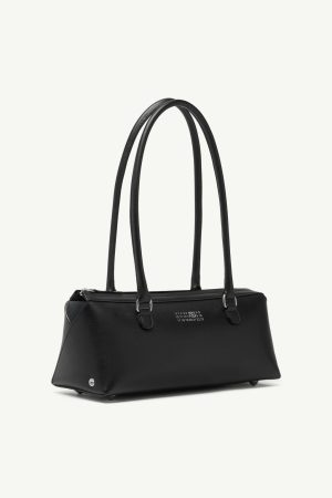 Black leather handbag with double top handles and subtle silver hardware, set against a pale background.