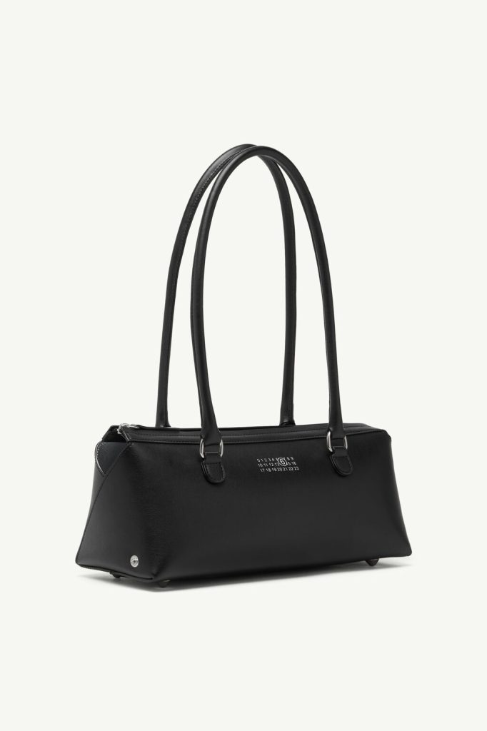 Black leather handbag with double top handles and subtle silver hardware, set against a pale background.