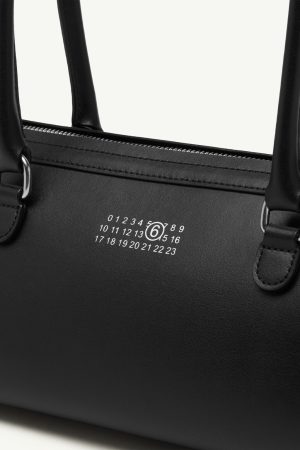 Close-up of a black leather handbag with a white calendar-style emblem and circular logo near the zipper.
