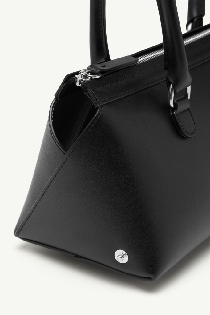Close-up of a black leather handbag with silver zip and hardware, showing the bottom corner and a metal stud.