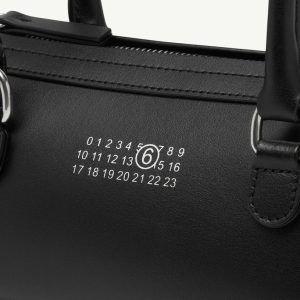 Close-up of a black leather bag showing a numeric dial with circled 6 on the surface, part of a security lock.