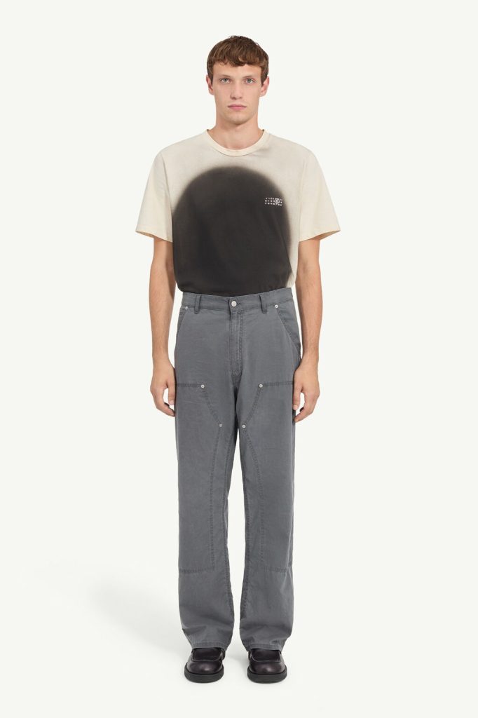 Male model wearing a beige T-shirt with a black gradient circle design and gray cargo pants, standing facing forward.