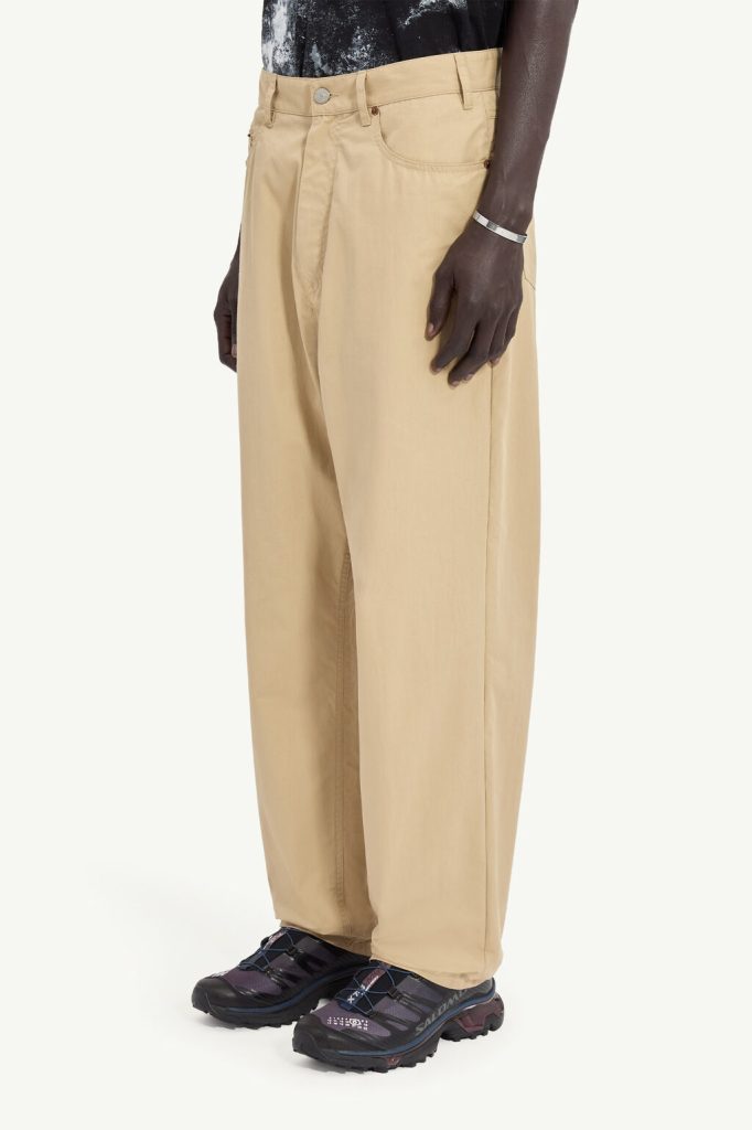 Side view of a person wearing beige wide-leg pants and dark hiking shoes, with a black patterned top partially visible.