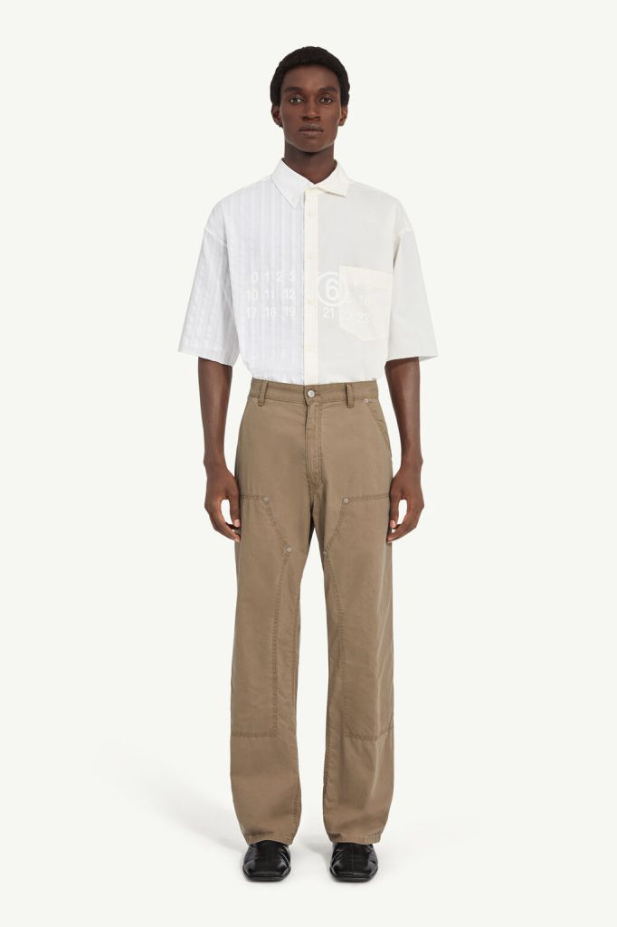 Male model wearing a white short-sleeve button-down shirt with beige cargo pants, standing facing forward with hands at his sides.