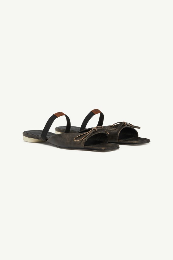 Dark brown leather slide sandals with black fabric back straps and tan lace details on a light background