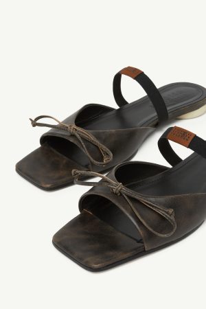 Brown distressed-leather sandals with square toes, lace-up fronts, and a black elastic back strap on a light background.