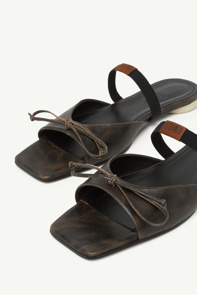 Brown distressed-leather sandals with square toes, lace-up fronts, and a black elastic back strap on a light background.