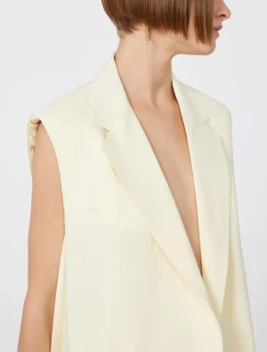 Cream sleeveless blazer with wide lapels on a model, shown in side profile.