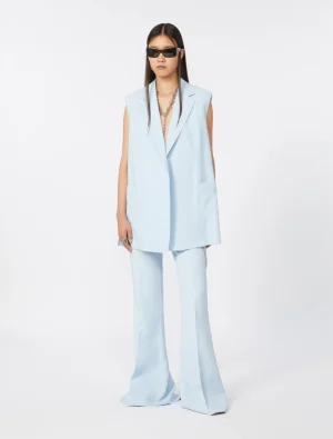 Model wearing a pale blue sleeveless blazer and matching wide-leg pants, accessorized with black sunglasses and a chunky silver chain necklace.