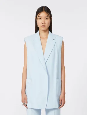 Woman wearing an oversized light blue sleeveless blazer with long lapels and front pockets in a studio.