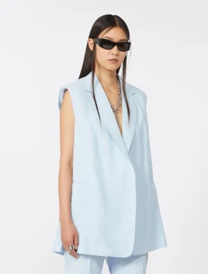 Model wearing a pale blue sleeveless blazer with matching trousers, black rectangular sunglasses, and a chunky silver necklace.