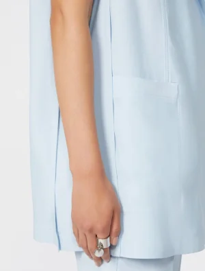 Close-up of a light blue coat sleeve with a front pocket and a hand wearing a silver ring.