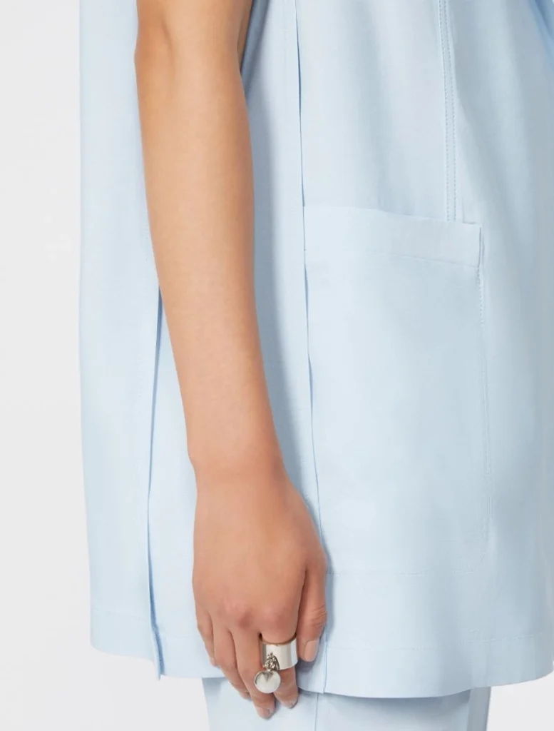 Close-up of a light blue coat sleeve with a front pocket and a hand wearing a silver ring.