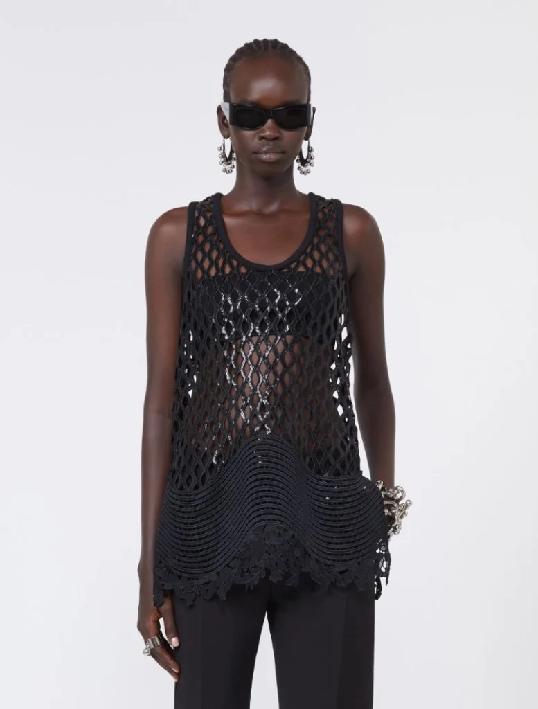 Model wearing a black fishnet sleeveless top over a bralette with oversized sunglasses and silver jewelry.