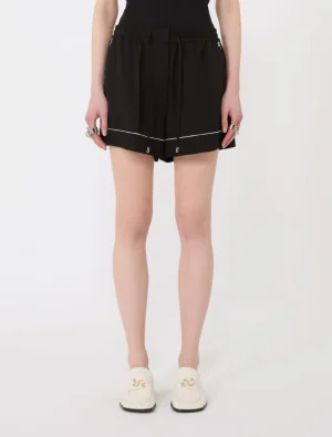 Black athletic-style shorts with an elastic drawstring and white piping, paired with white loafers, shown from the waist downening the legs.