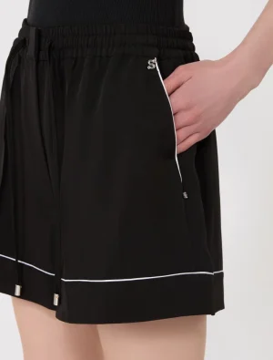 Close-up of black athletic shorts with white piping, an elastic waistband, and a hand resting in a side pocket.