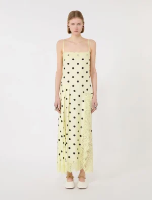 Young woman wearing a pale yellow spaghetti-strap maxi dress with black polka dots and lace trim at the hem, standing against a light background.